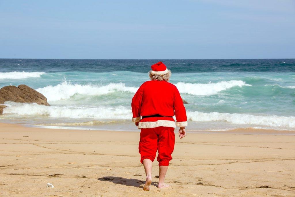Santa in red dress shirt and brown shorts standing on beach during daytime