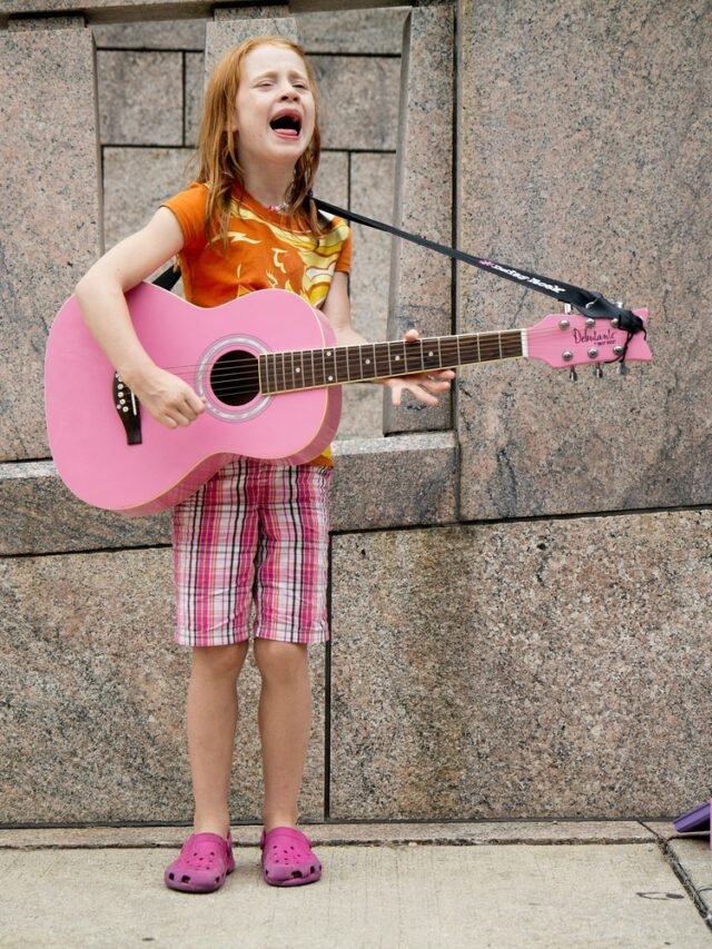 a kid girl is singing on road by wearing pink dress