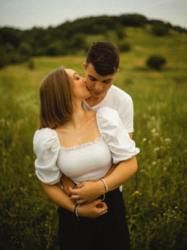 woman in white long sleeve shirt kissing man in black shirt on green grass field during