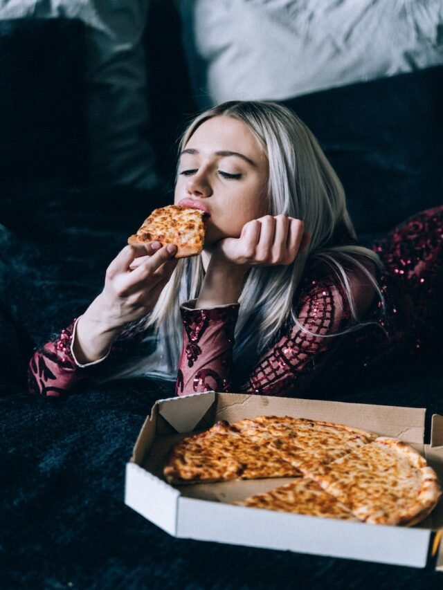 woman in red and black plaid long sleeve shirt eating pizza
